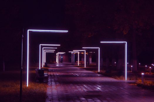 A moody illuminated pathway featuring modern neon lights in a peaceful park setting.